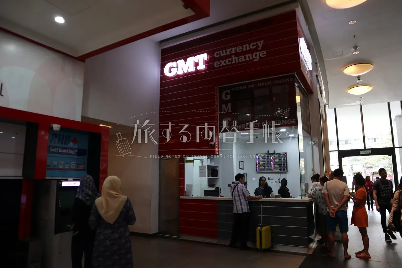 NU Sentral モール内の赤いキオスク型両替店 GMT currency exchange に並ぶ利用客と隣接する RHB Self Banking ATM