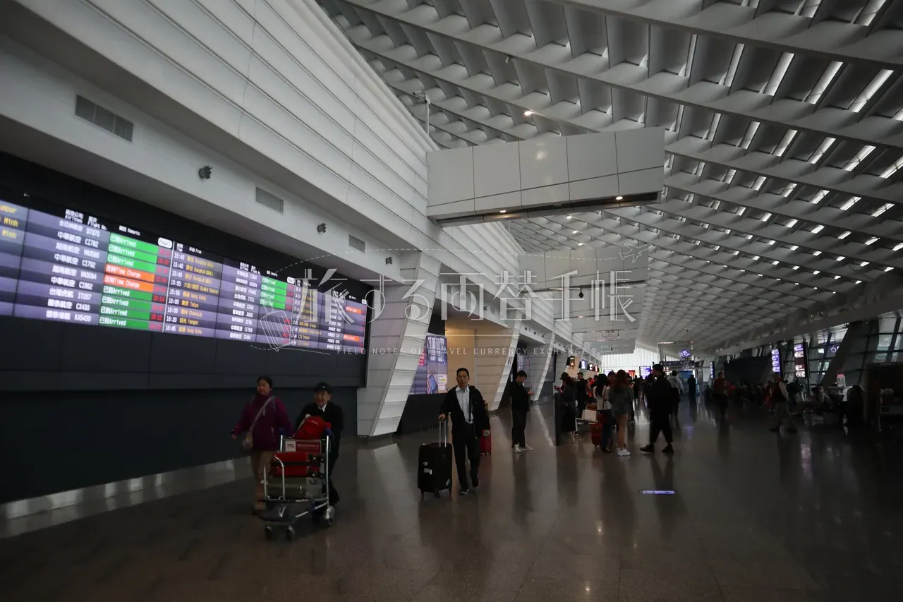 桃園空港到着ロビー、フライト掲示板と荷物カートを押す旅行者