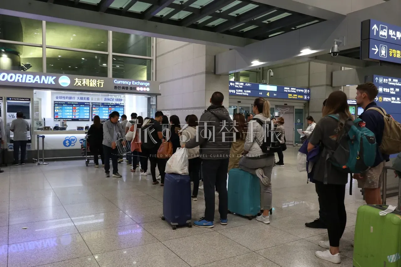 仁川空港のウリィ銀行両替カウンター前に並ぶスーツケースを引いた旅行者15名以上の長い行列