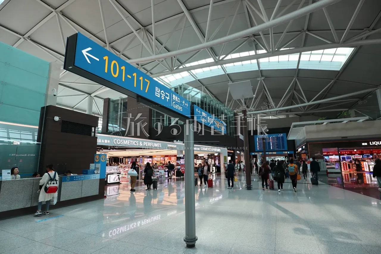 仁川空港出国エリアの天井から吊り下げられた巨大な青地ゲート案内サイン「101-117 탑승구 搭乗口 ゲート」と免税店通路