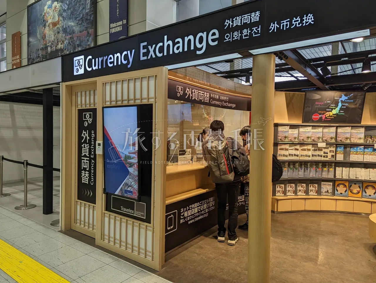 博多駅構内の和風木格子調 Currency Exchange カウンターで両替手続き中の観光客