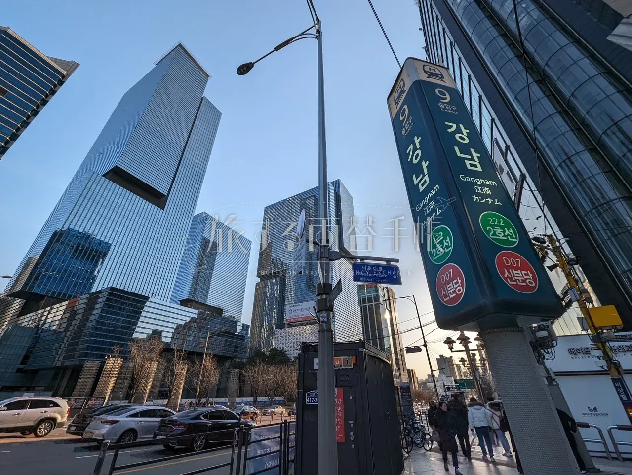 ソウル地下鉄2号線「강남 / Gangnam / 江南」駅の縦長案内サインと奥の三角形高層ビル群