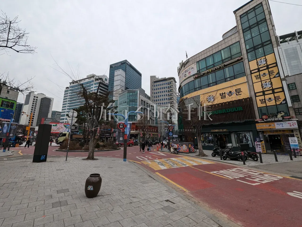 ソウル中心部の広場と歩道。曇天の中、観光客向け店舗が並ぶ通りの広角ショット