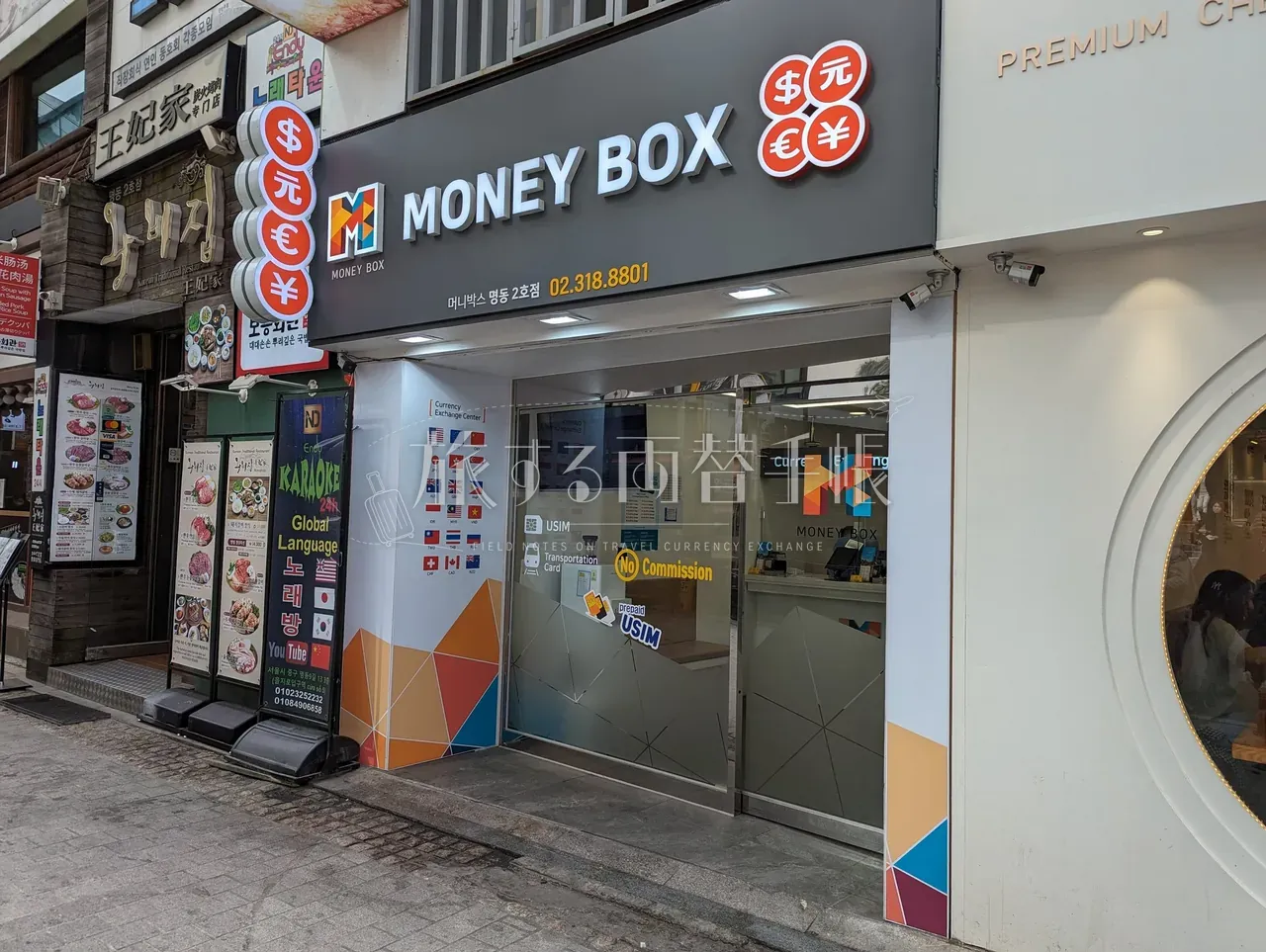 明洞のMoney Box店舗外観。黒地に白文字の看板と橙色のMロゴ、$元€¥通貨記号ラベル
