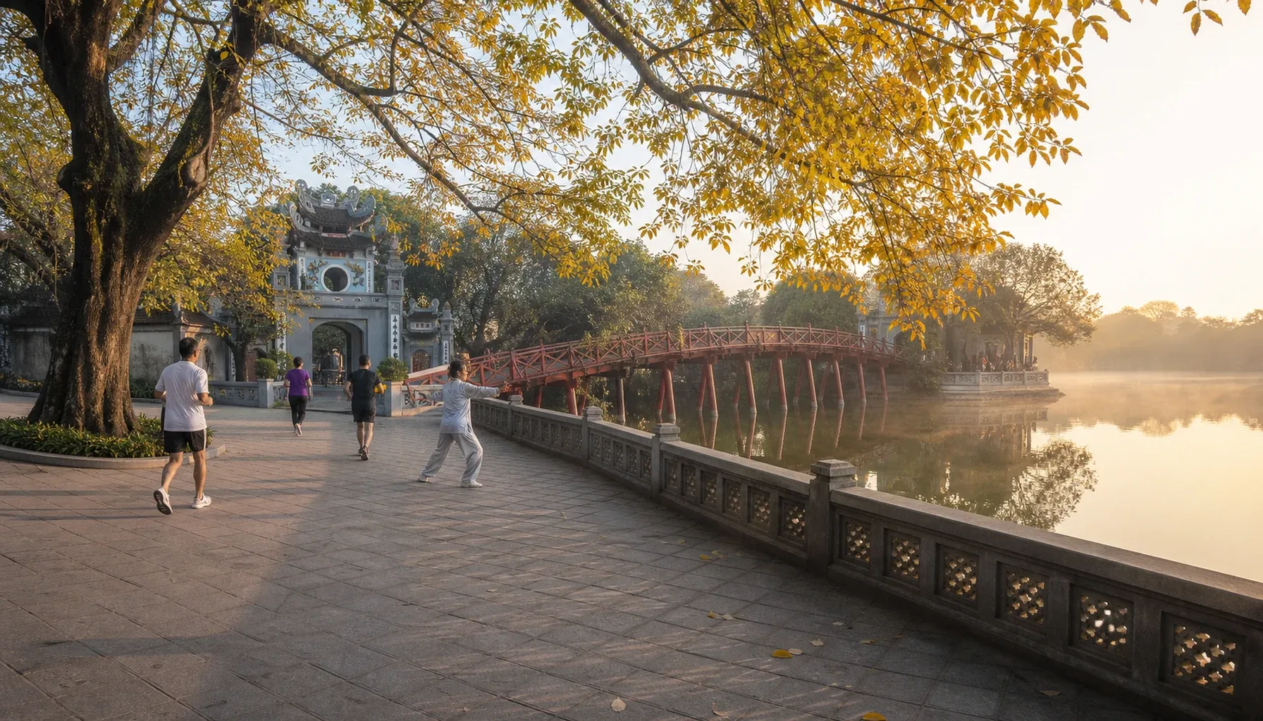 ハノイ・ホアンキエム湖の朝景。赤い The Huc Bridge と玉山祠（Ngoc Son Temple）が中央に見え、湖面の靄と紅葉の銀杏が周囲を囲む。